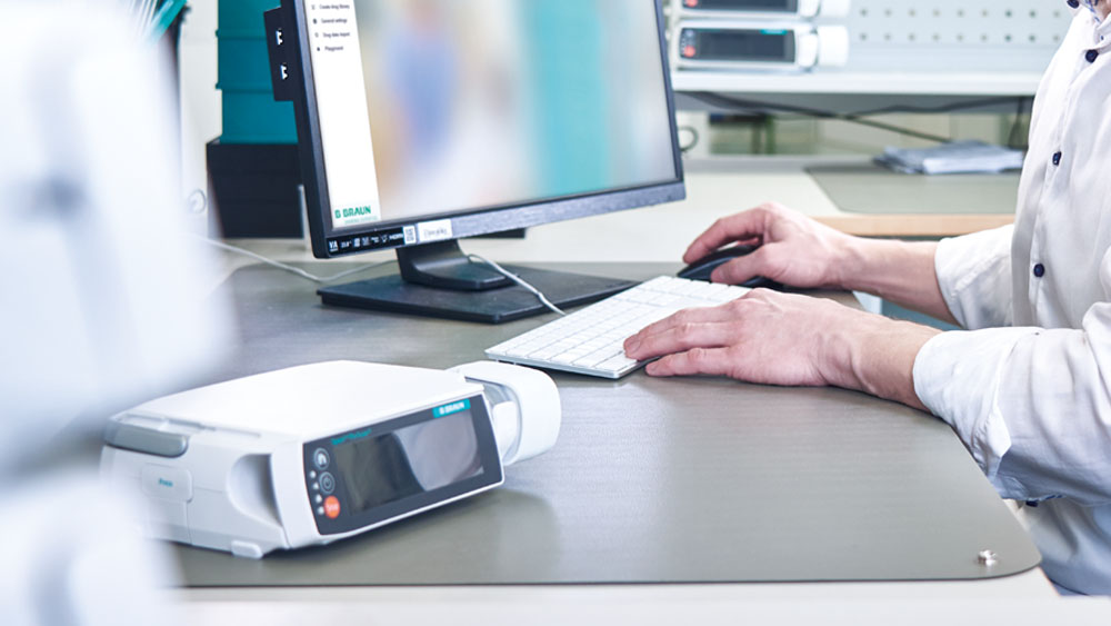 Biomed bilgisayar önünde oturuyor. Ön planda bir B. Braun infüzyon pompası bulunmaktadır.