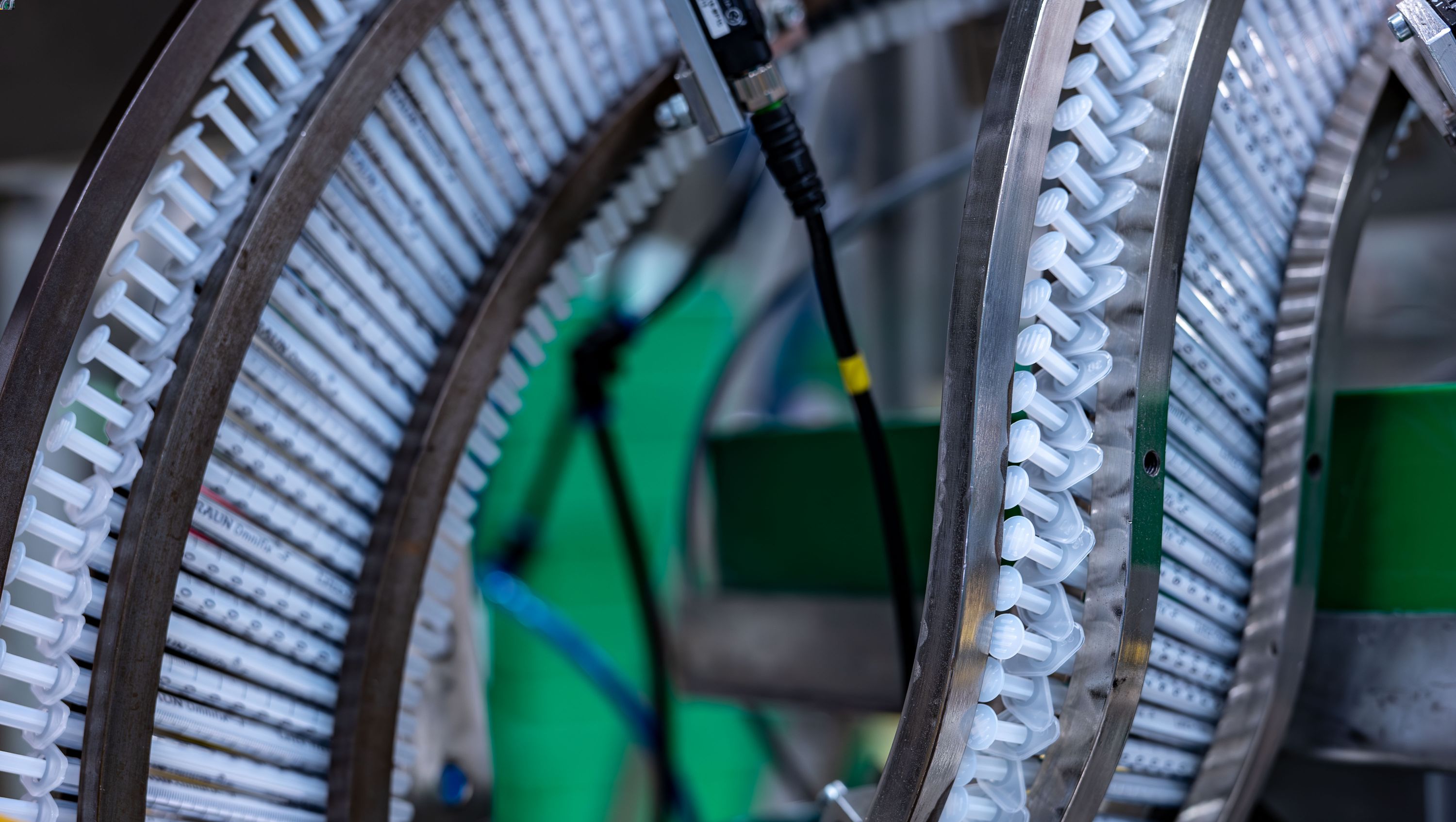 Üretim ortamında arka arkaya dizilmiş birçok şırınga. Bu, bir ürünün ham madde tedarikinden imhasına kadar toplam çevresel etkisini belirlemek için ürün yaşam döngüsünü analiz etmemizi simgelemektedir. 