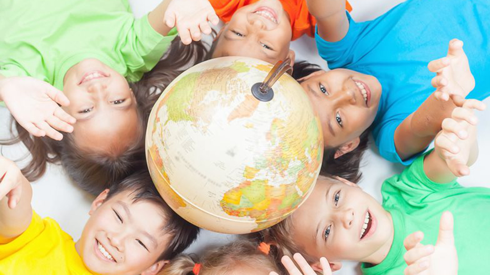 Kollarını yukarı doğru uzatırken zeminde bir küre etrafında yatan gülümseyen çocuklar.